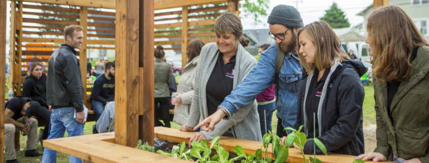 A professor and three students admire plants growing in a large wooden box.