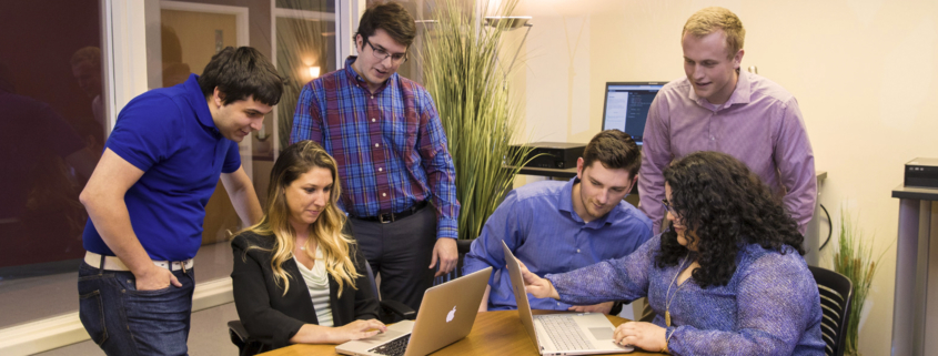 Several computer science students are seated at a table while looking at laptop computers