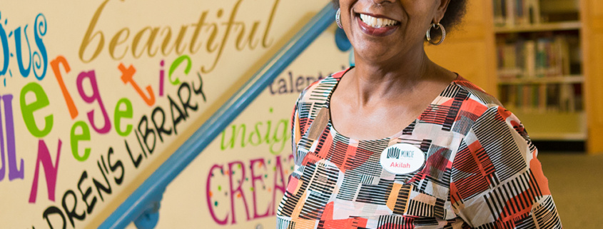 A library employee poses for a photo in front of a colorful wall with a mural of words.