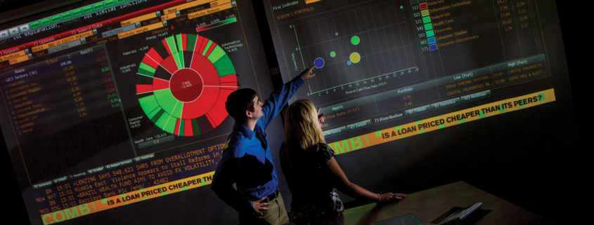 Photo shows two people pointing at monitors in the the A. Umit Taftali Center for Capital Markets and Investing.