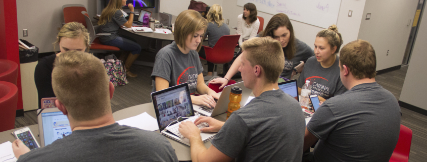 Several students sit at a table with their laptop computers