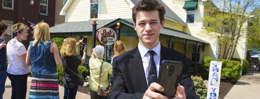 A student is holding a mobile phone outside of a Carmel business