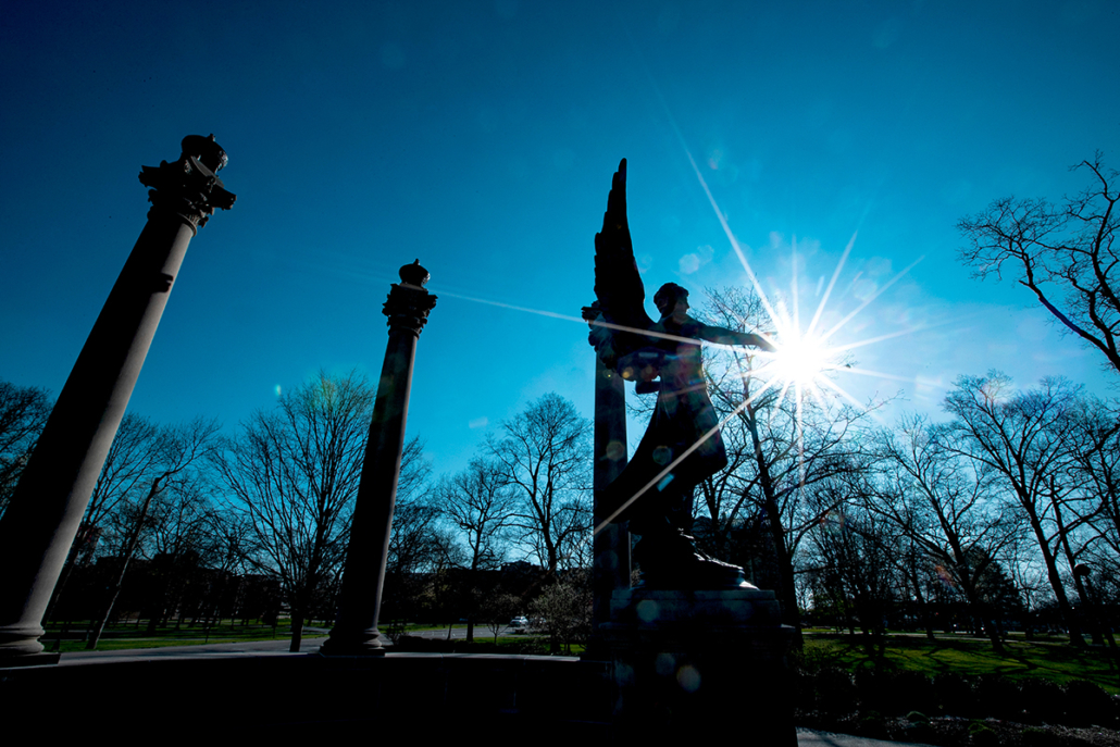 The Beneficence statue and three columns are surrounded by blue skies and a star-shaped sun flare