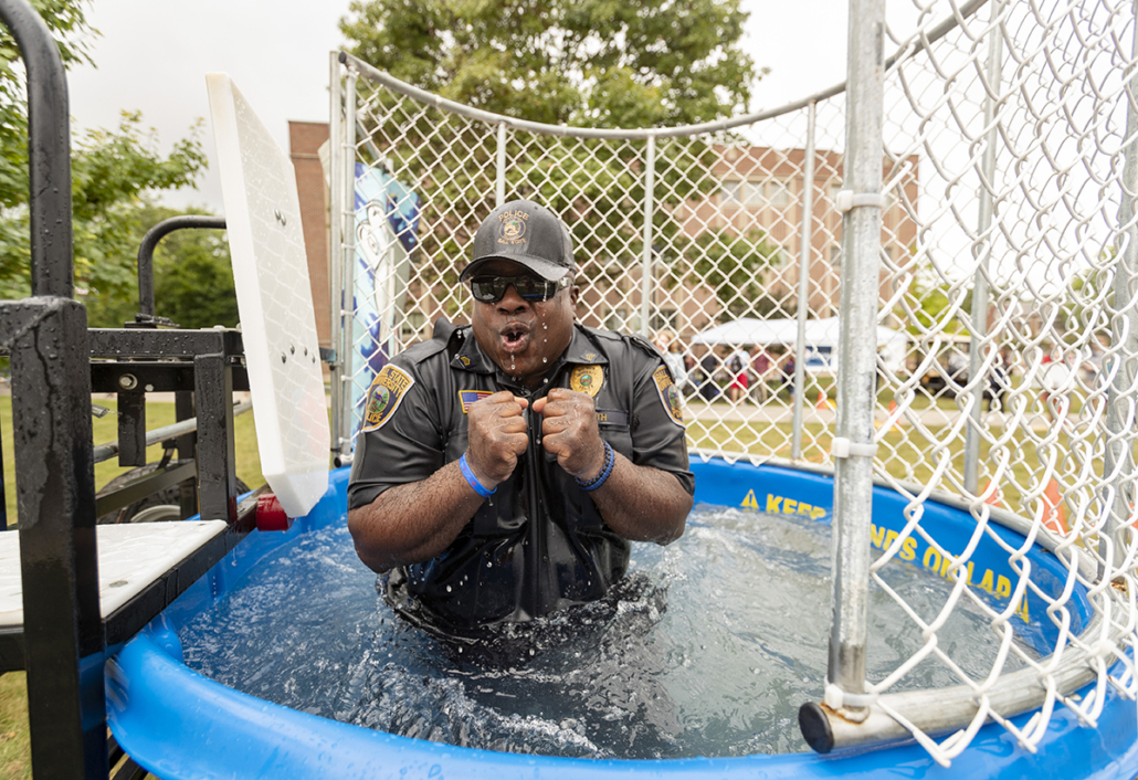 A Ball State police officer in uniform, shivering while standing waist-deep in water in a dunk tank