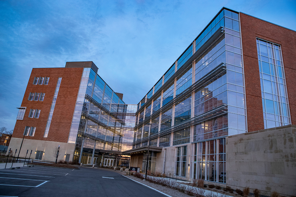 A glass-front multi-story building surrounded by an evening blue sky